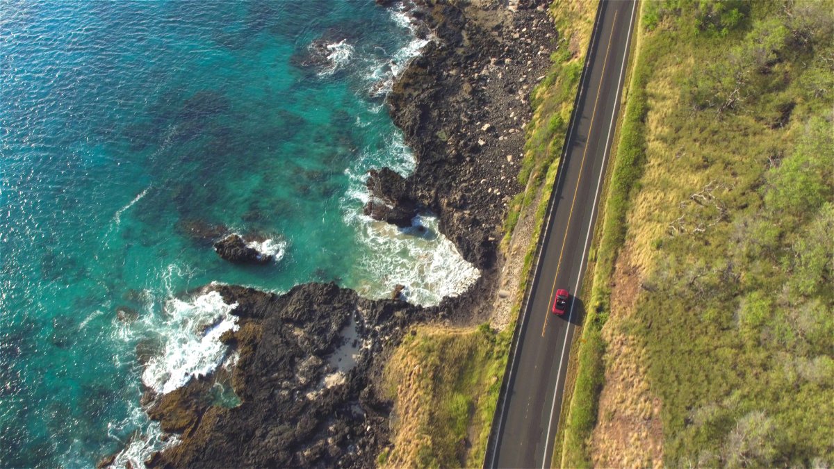 AERIAL: Red convertible driving on amazing coastal road above rocky ocean cliffs
