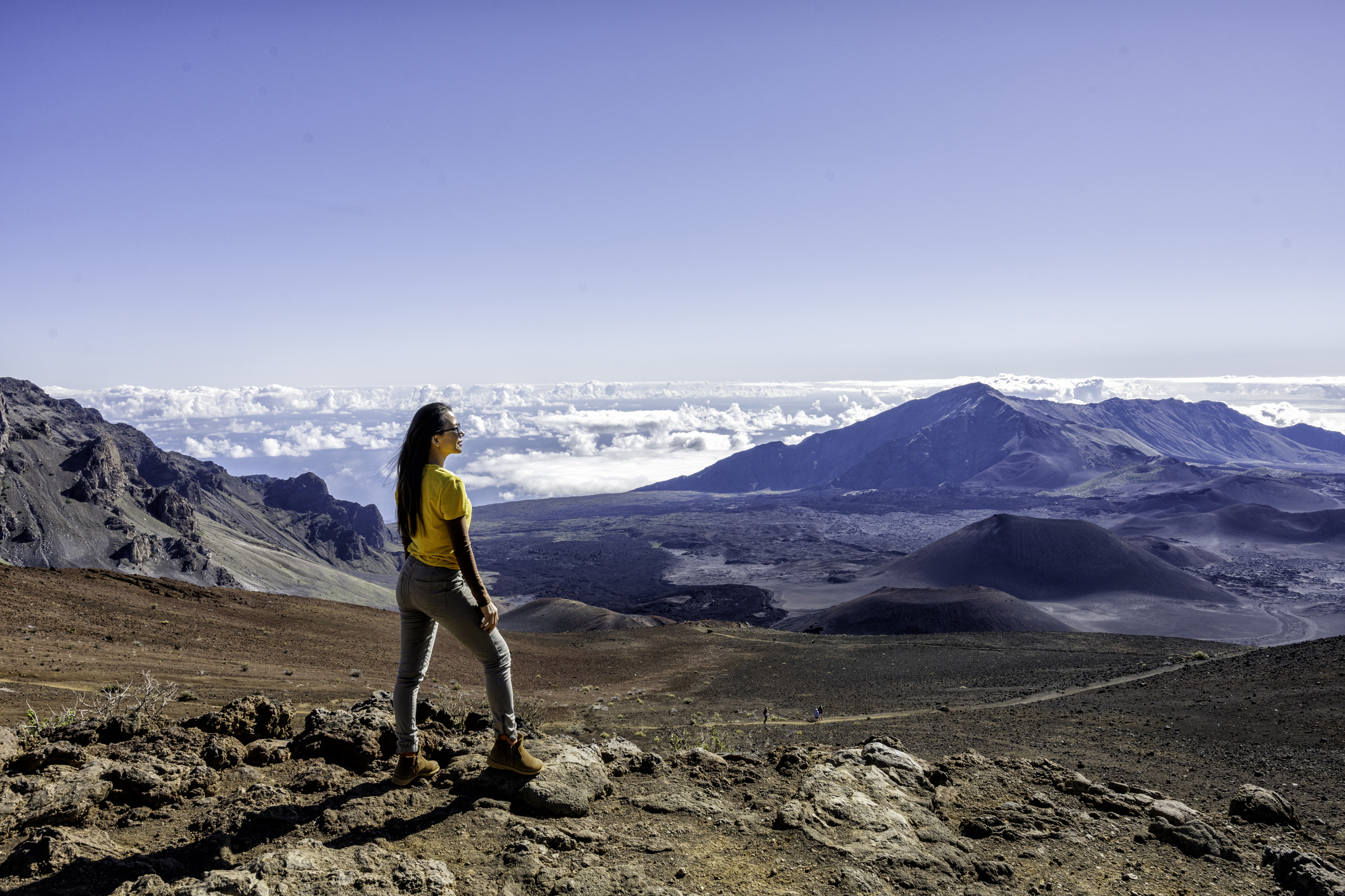 Traveling woman standing on the top of Haleakala mountain over sunrise sky and over volcano mountains view.