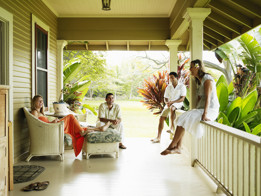 Group of friends sitting on front porch of tropical home laughing